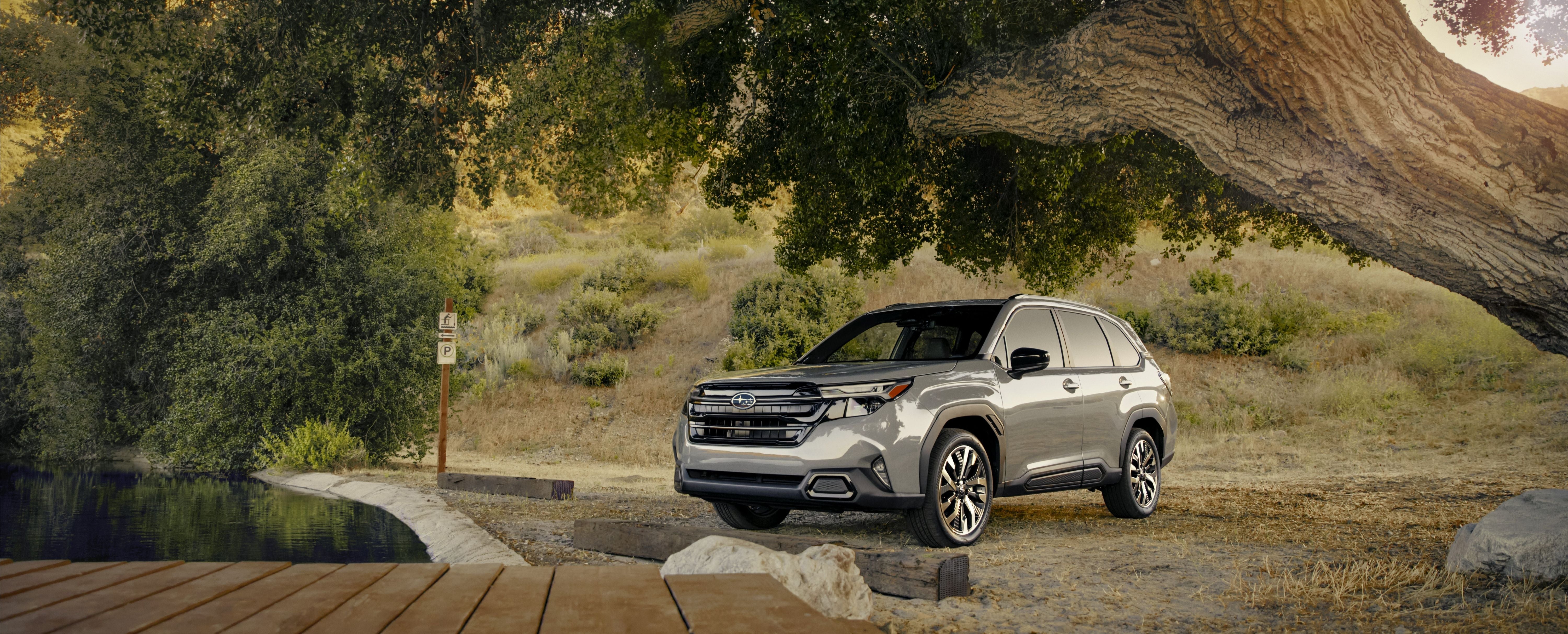 a 2025 subaru forester parked next to a pond with a park bench in front and a large tree overhanging.