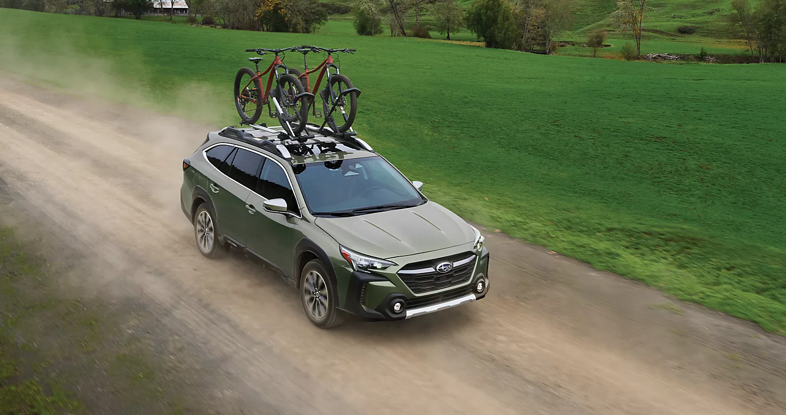 A green suv driving on a dirt road with two bikes attached to the roof.