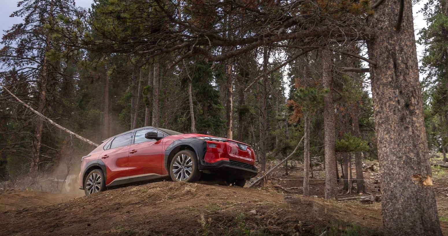 A red and black 2026 Subaru Solterra site majestically driving on a road surrounded by evergreens.