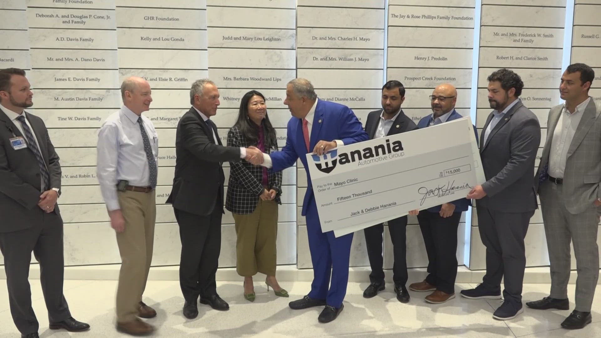 Hanania Automotive Group presents a donation check to Jacksonville hospital leaders in front of a donor recognition wall
