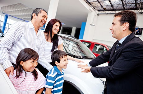 a family at a car dealership with a salesman looking at a white vehicle